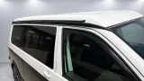 Spoilerset en multirail langs de dakrand van een witte camper tegen de grijze wand