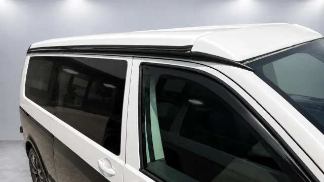 Spoilerset en multirail langs de dakrand van een witte camper tegen de grijze wand