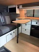 Zit/slaapbank met tafel en keuken in een camperinterieur